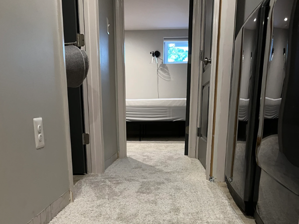 Home hallway with carpet installed near launder room and a bedroom at the end of the hall.